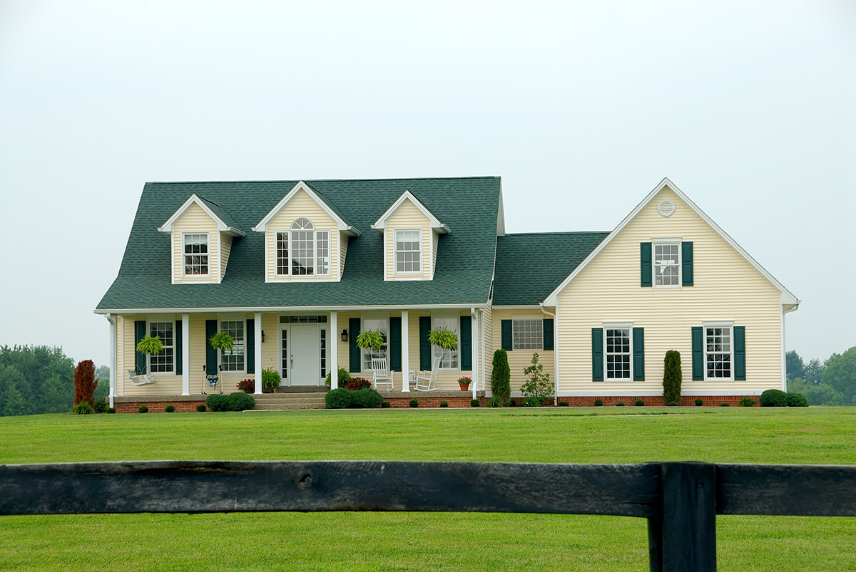 A,Two,Story,Vinyl,Sided,Farmhouse,Sits,On,The,Manicured Large yellow home with a large yard.