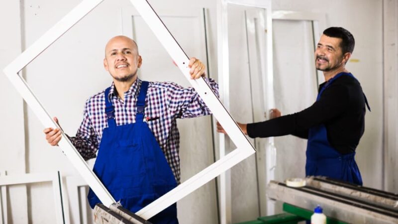 Two installation technicians carry replacement windows into room